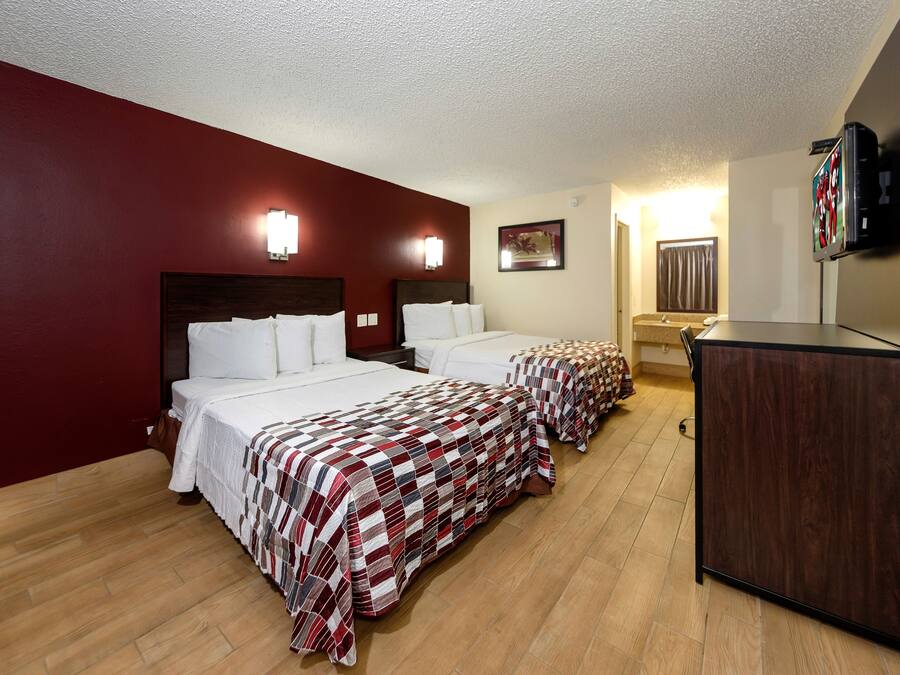 A hotel room with two beds, a television, and a desk.