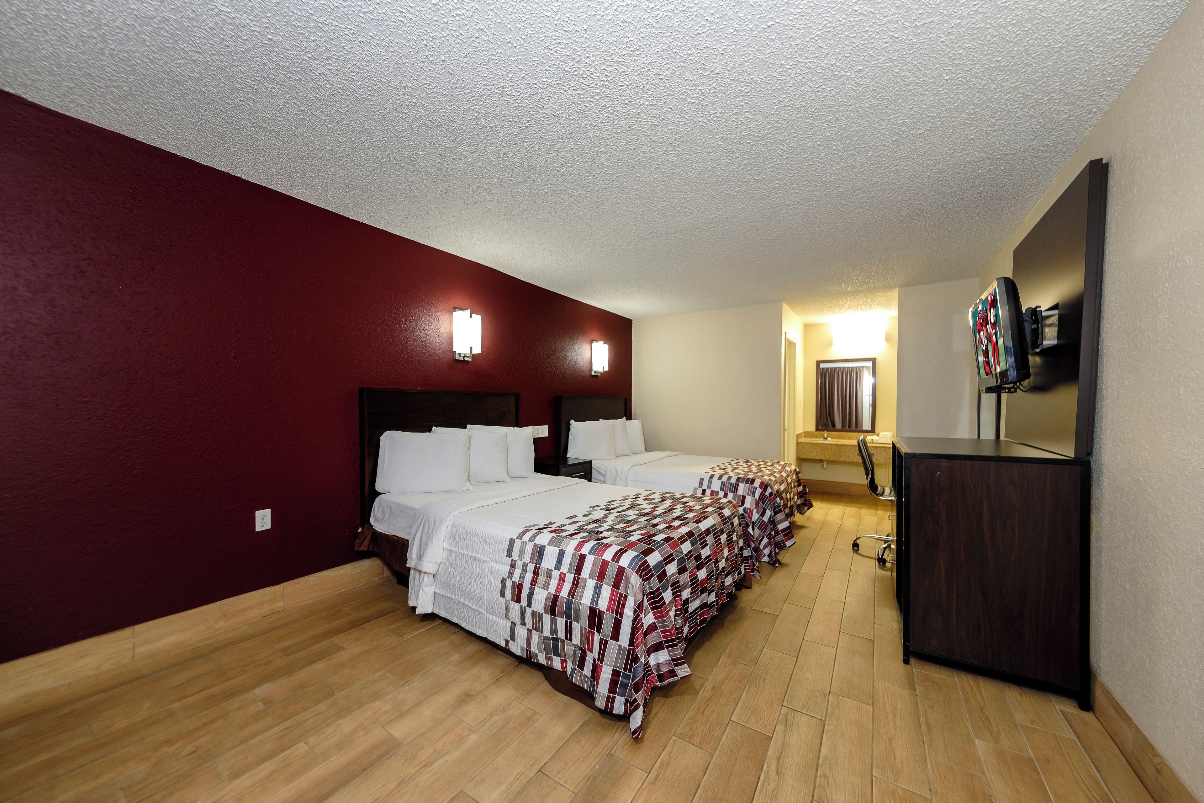 A hotel room with two beds, a desk, a mirror, and a television.