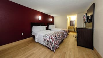 A hotel room with two beds, a desk, a mirror, and a television.