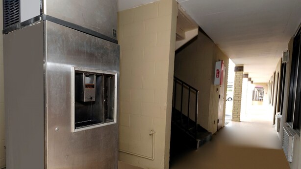 Un pasillo con una máquina expendedora, una escalera y una puerta que da a otra habitación.