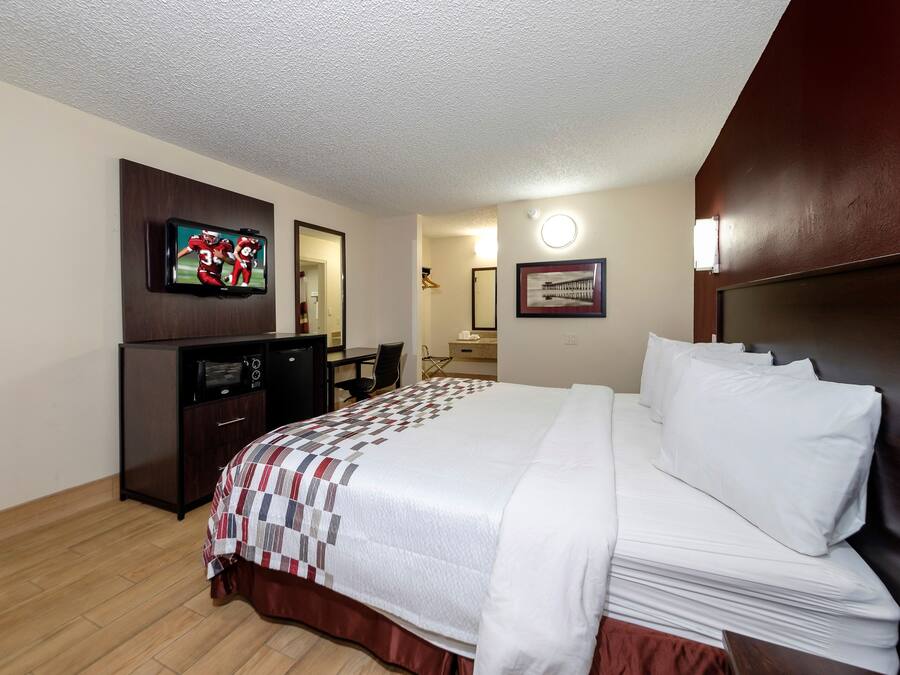 A hotel room with a bed, a desk, a television, a mirror, and a picture on the wall.