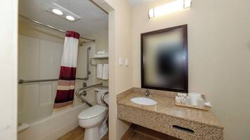 A bathroom with a toilet, grab bars, a shower with a red and white curtain, a sink with a tray of toiletries, and a mirror.