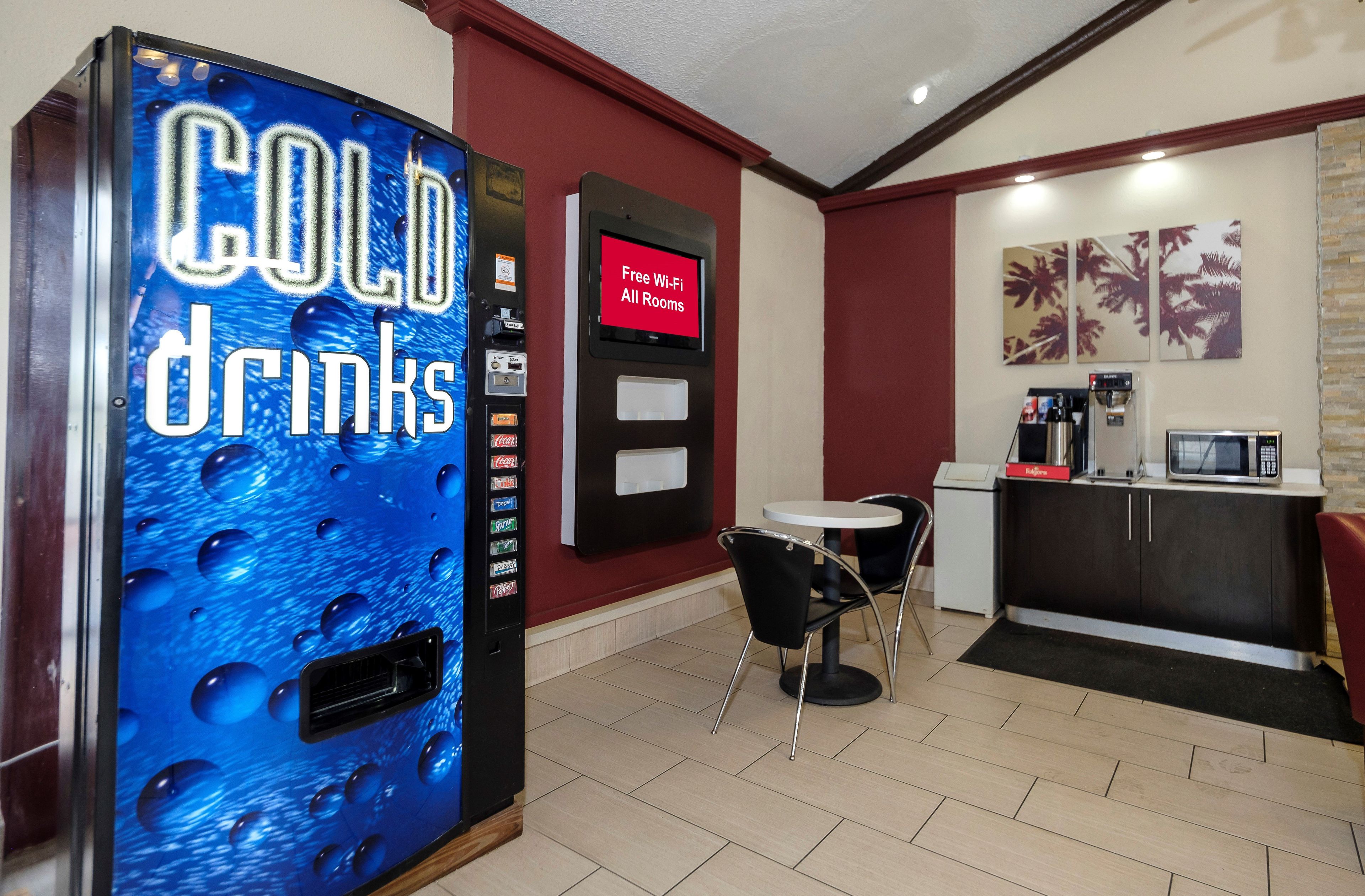 A vending machine for cold drinks, a digital display for free Wi-Fi, a small table with chairs, and a microwave.