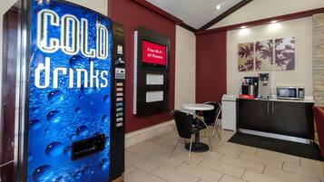 A vending machine for cold drinks, a digital display for free Wi-Fi, a small table with chairs, and a microwave.