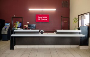 A reception desk with a flat-screen TV, an ATM, and a sign indicating free Wi-Fi in all rooms. - Red Roof Inn New Orleans - Westbank (Harvey)