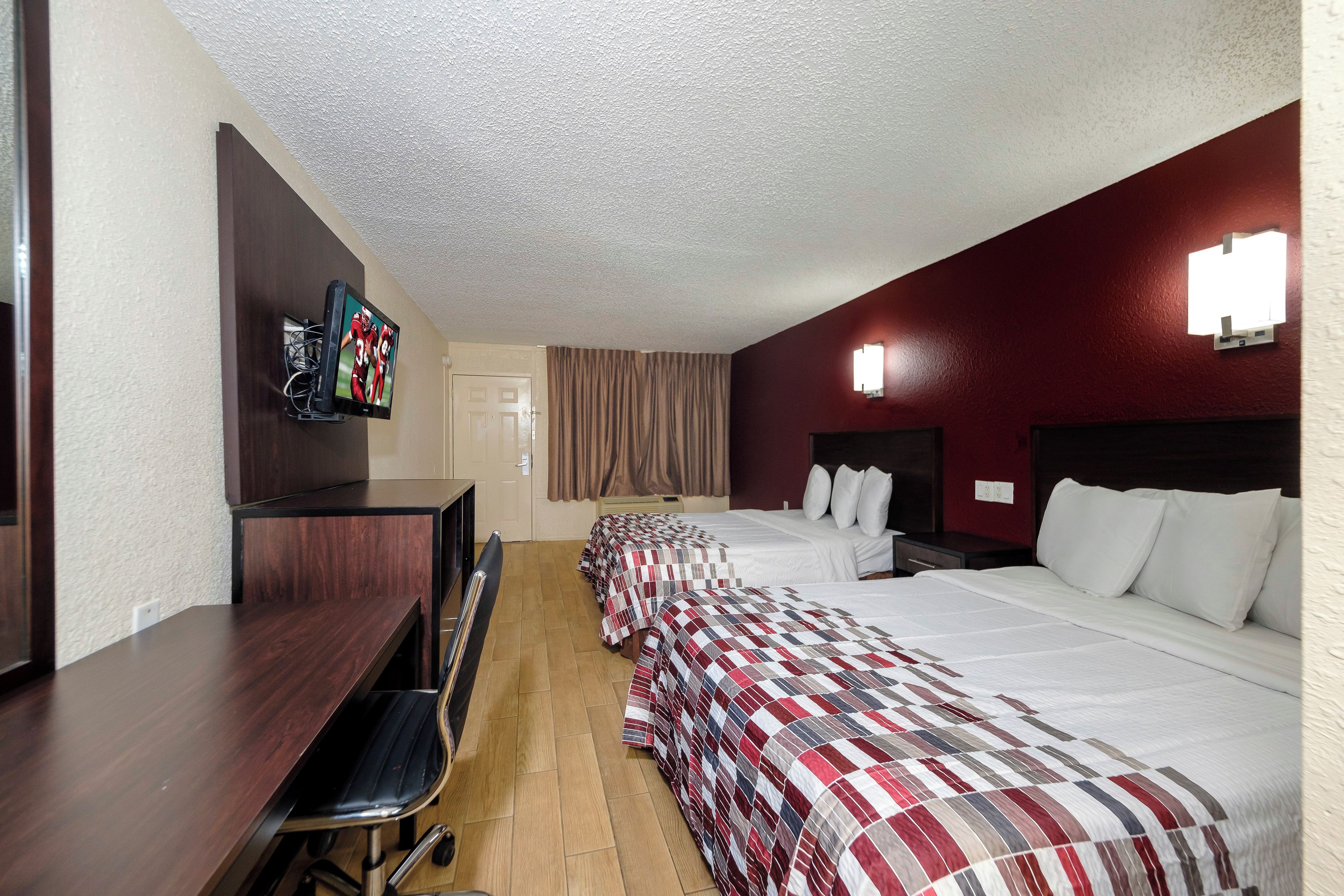 A hotel room with two beds, a desk, a chair, a television, and a bathroom door.