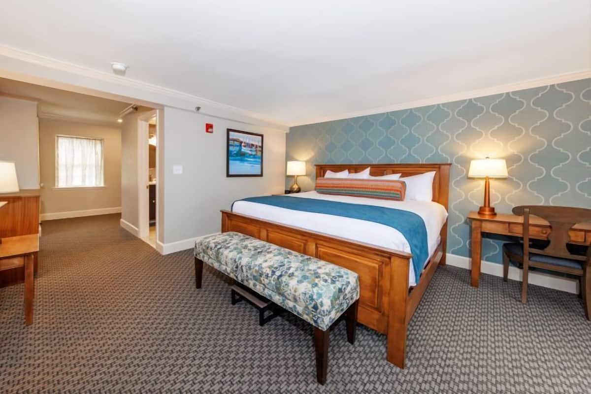A hotel room with a bed, a desk, a chair, a bench, and a bathroom visible through an open door.