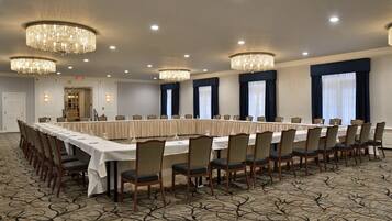 A conference room with a long table, chairs, chandeliers, and a carpeted floor.