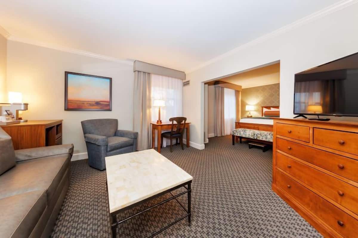 A hotel room with a sofa, a small table, a TV, a wooden dresser, and a bed with a patterned bedspread.