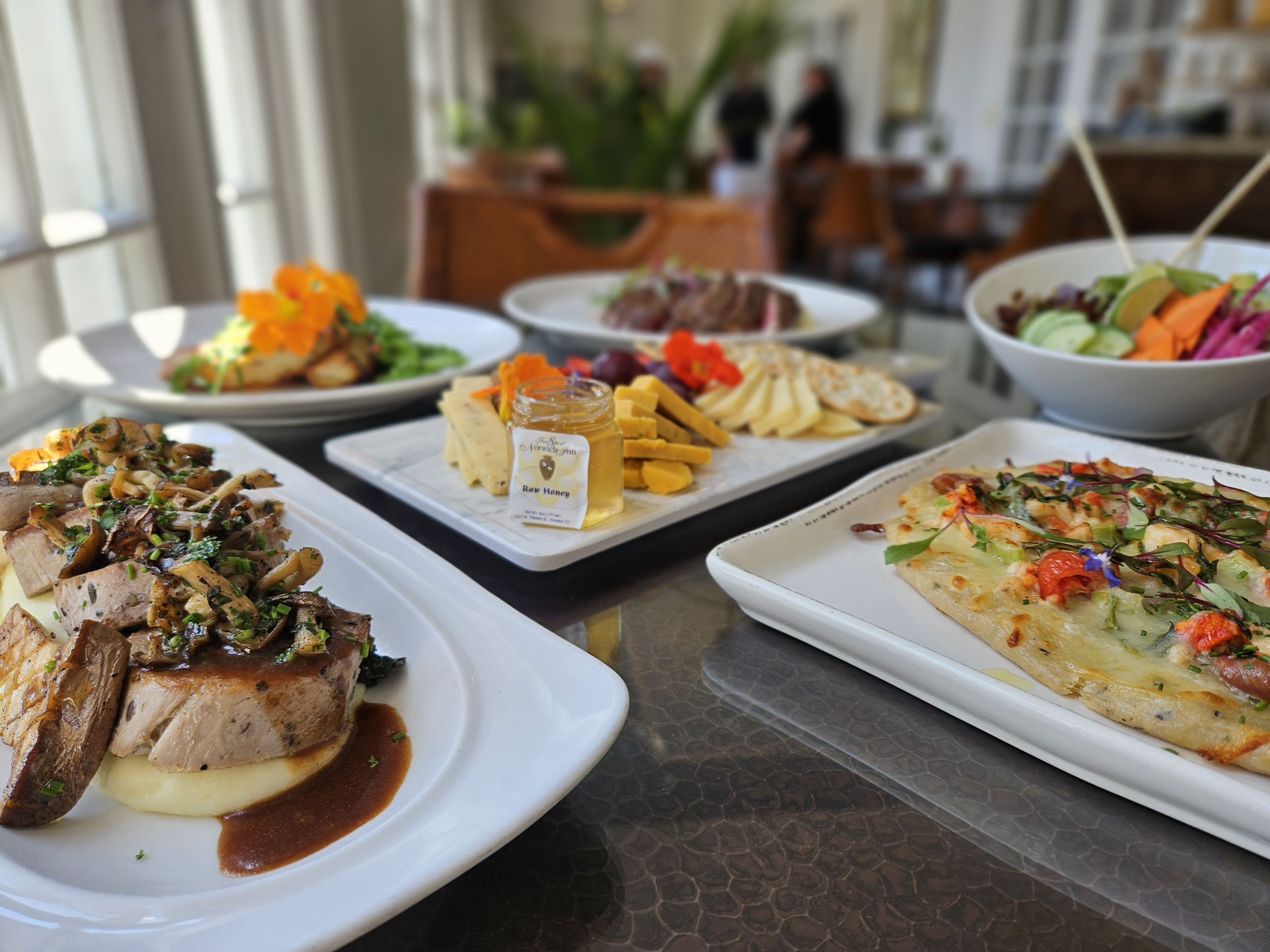 A variety of dishes on a table, including steak, fries, and a pizza.