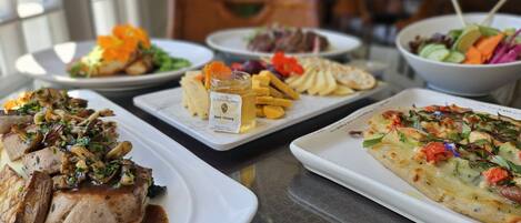 A variety of dishes on a table, including steak, fries, and a pizza.