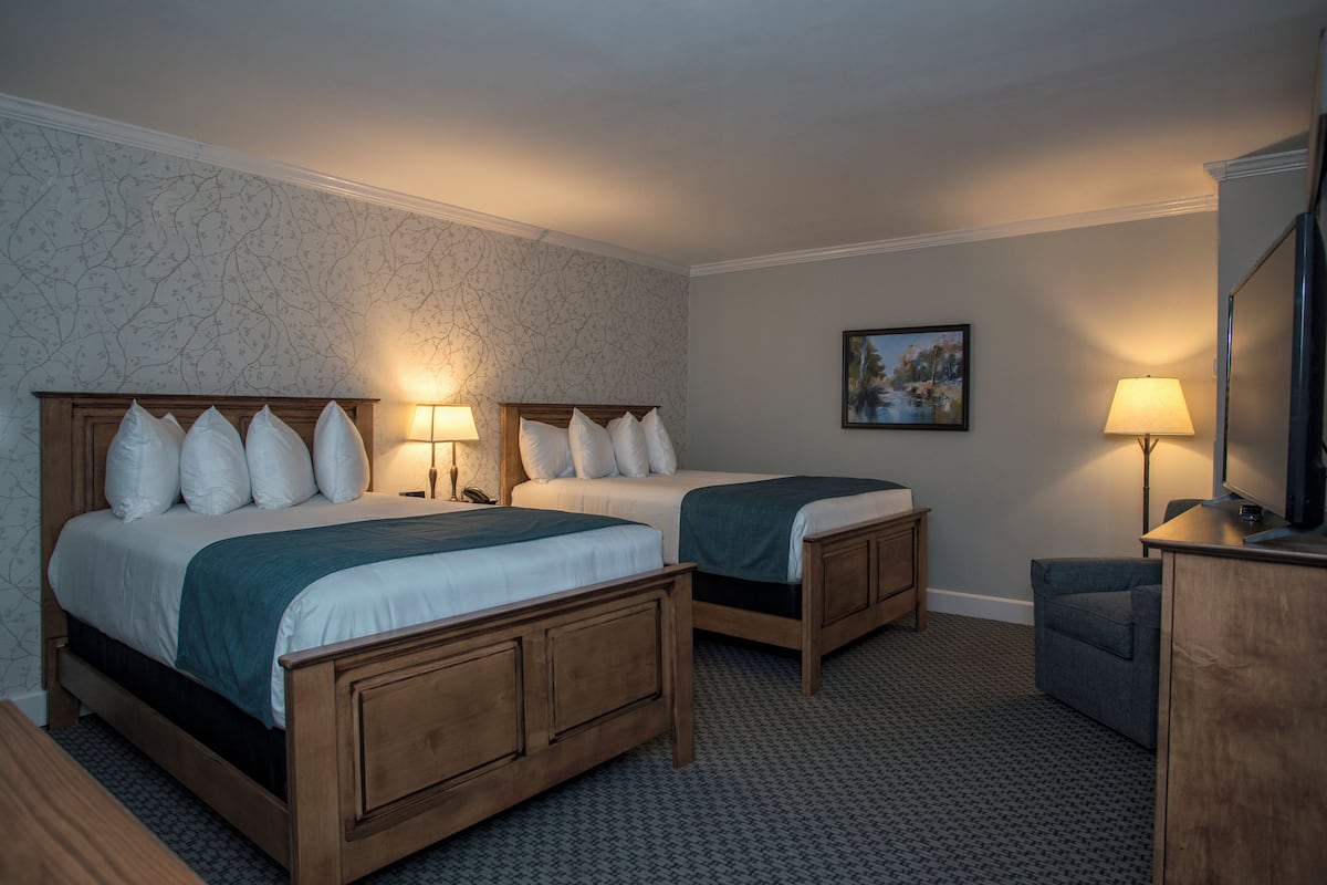 A hotel room with two wooden beds, a desk, and a chair.