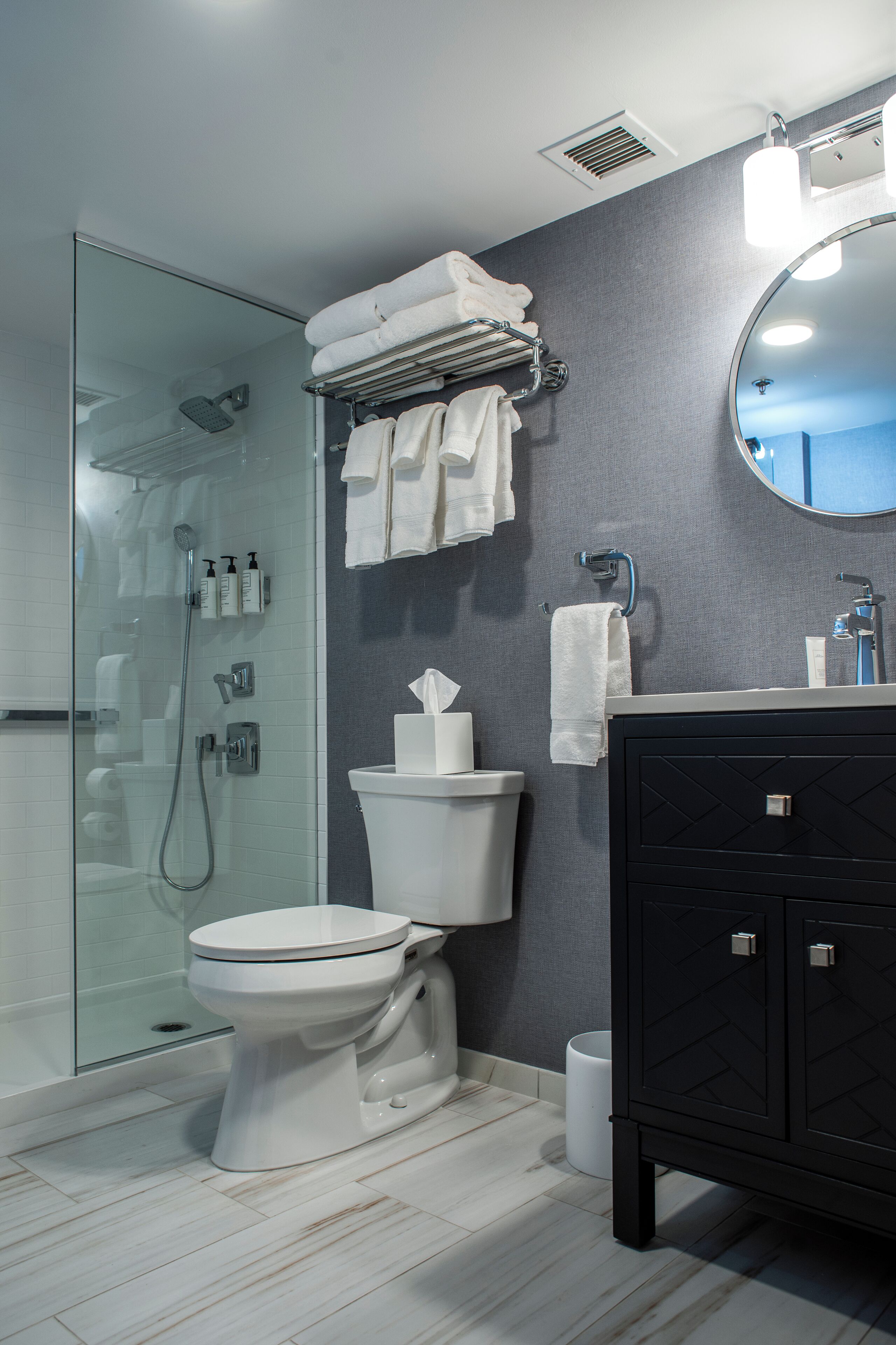 A modern bathroom with a glass-enclosed shower, a white toilet, a black vanity, and a mirror.