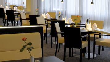 A restaurant with multiple tables and chairs, some with napkins and flowers.