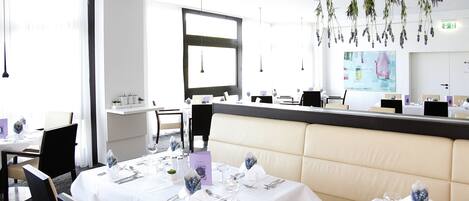 A dining area with white tablecloths, neatly set tables, and a modern chandelier.