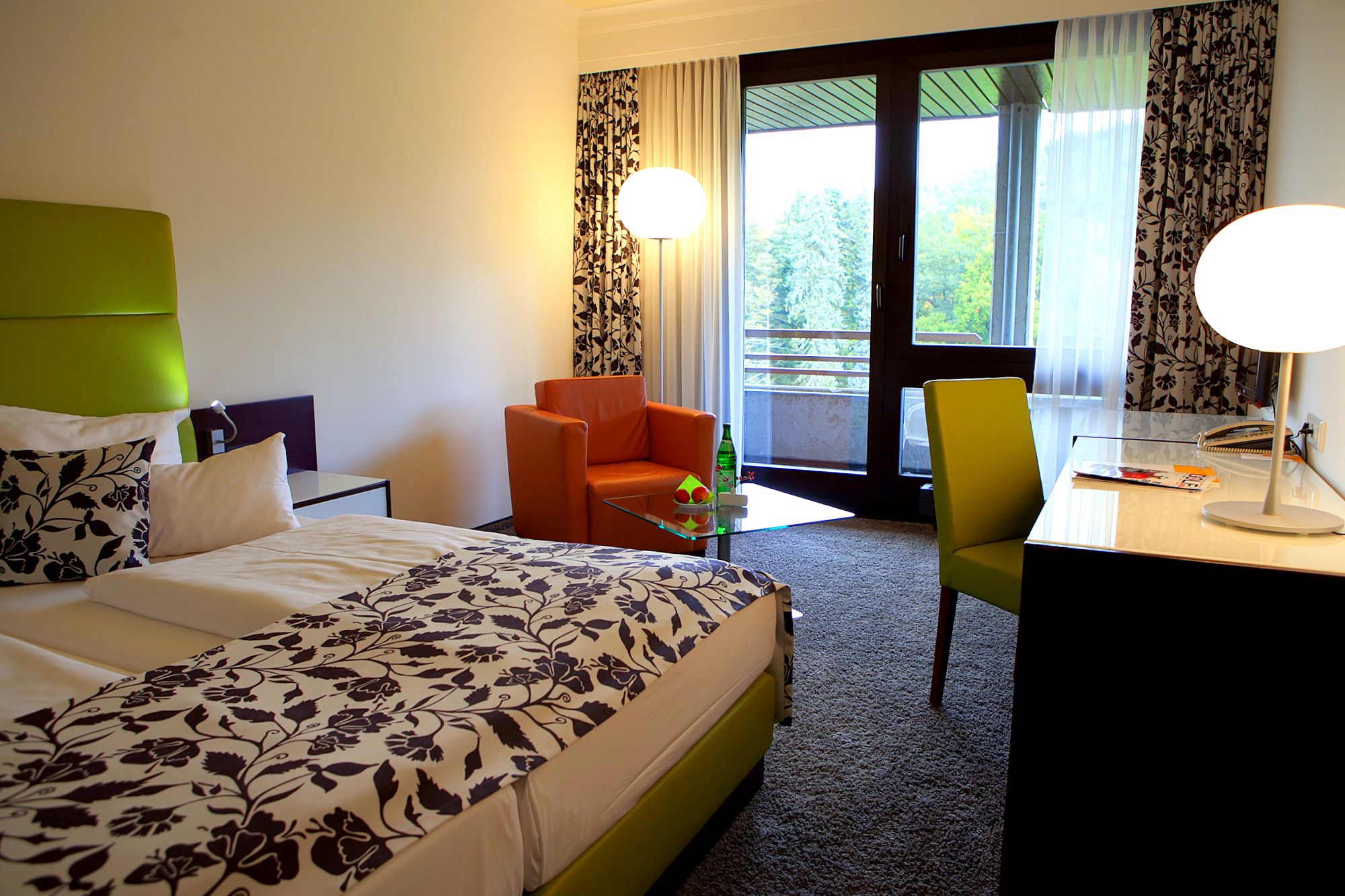 Une chambre d’hôtel avec un lit, un bureau, une chaise et un balcon avec des rideaux.