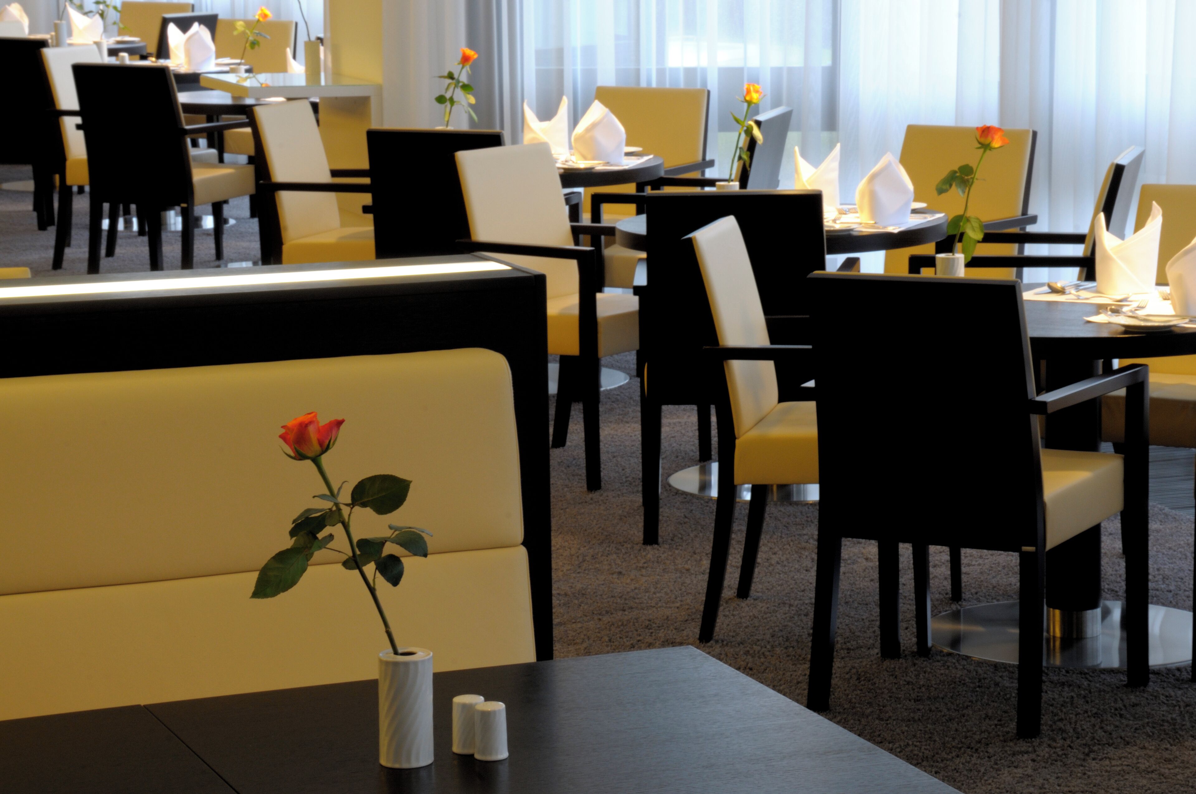 A hotel dining area with tables and chairs, some with flowers.