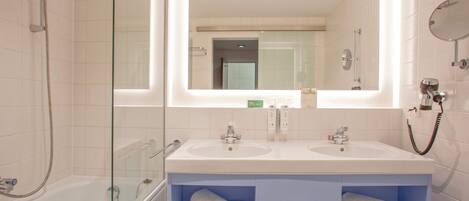 Een moderne badkamer met een glazen douchecabine, twee wasbakken en een grote spiegel boven het aanrecht.