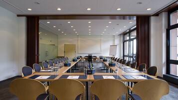 Ein Konferenzraum mit einem langen Tisch, Stühlen und einer Projektionsleinwand.