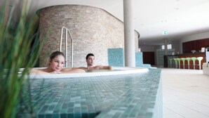 A modern indoor swimming pool with a curved stone wall and a bar area in the background. - Hotel an der Therme Bad Orb (Bad Orb)