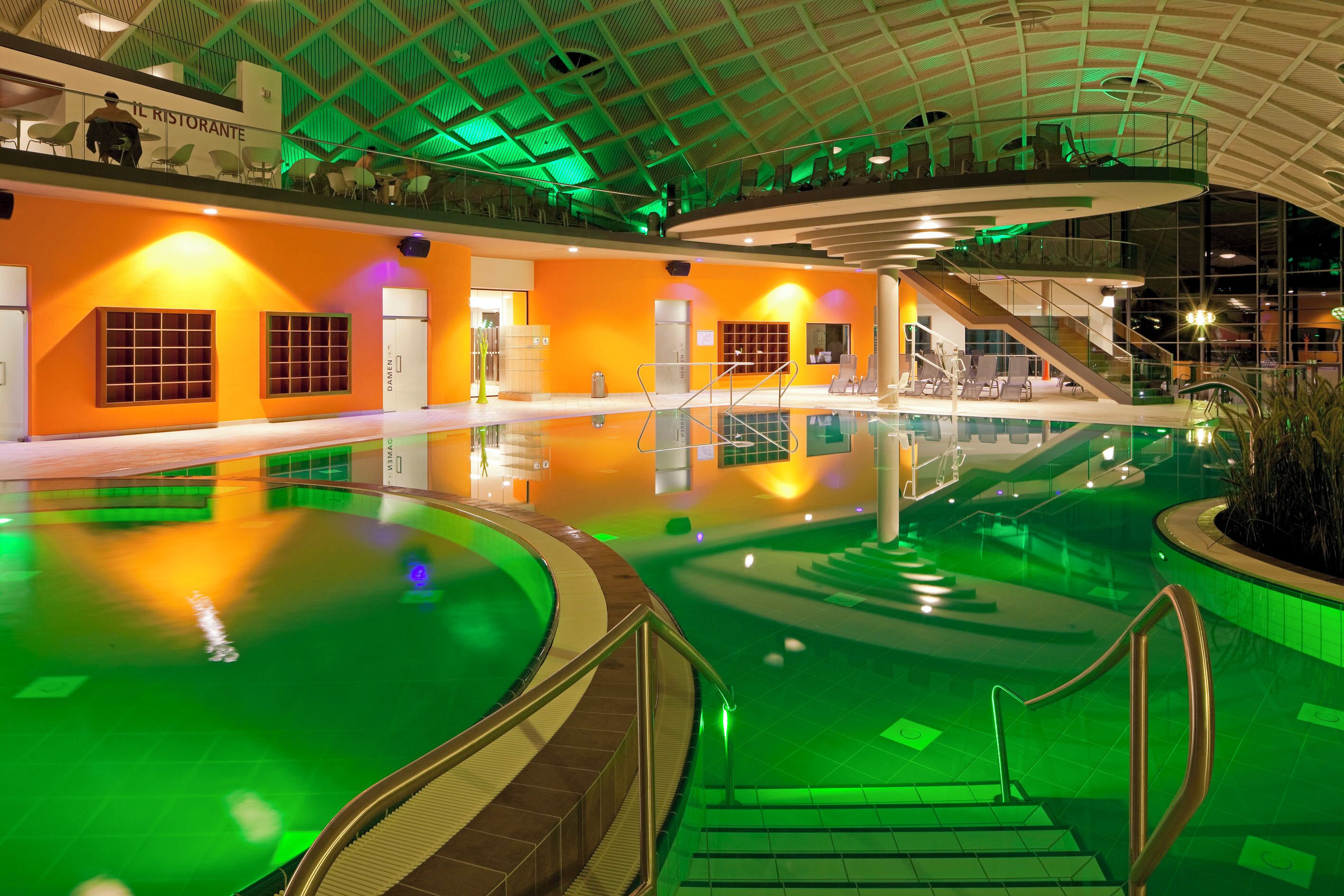 An indoor swimming pool with a glass ceiling, surrounded by orange walls and green lighting.