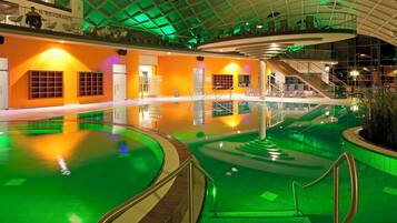 An indoor swimming pool with a glass ceiling, surrounded by orange walls and green lighting.