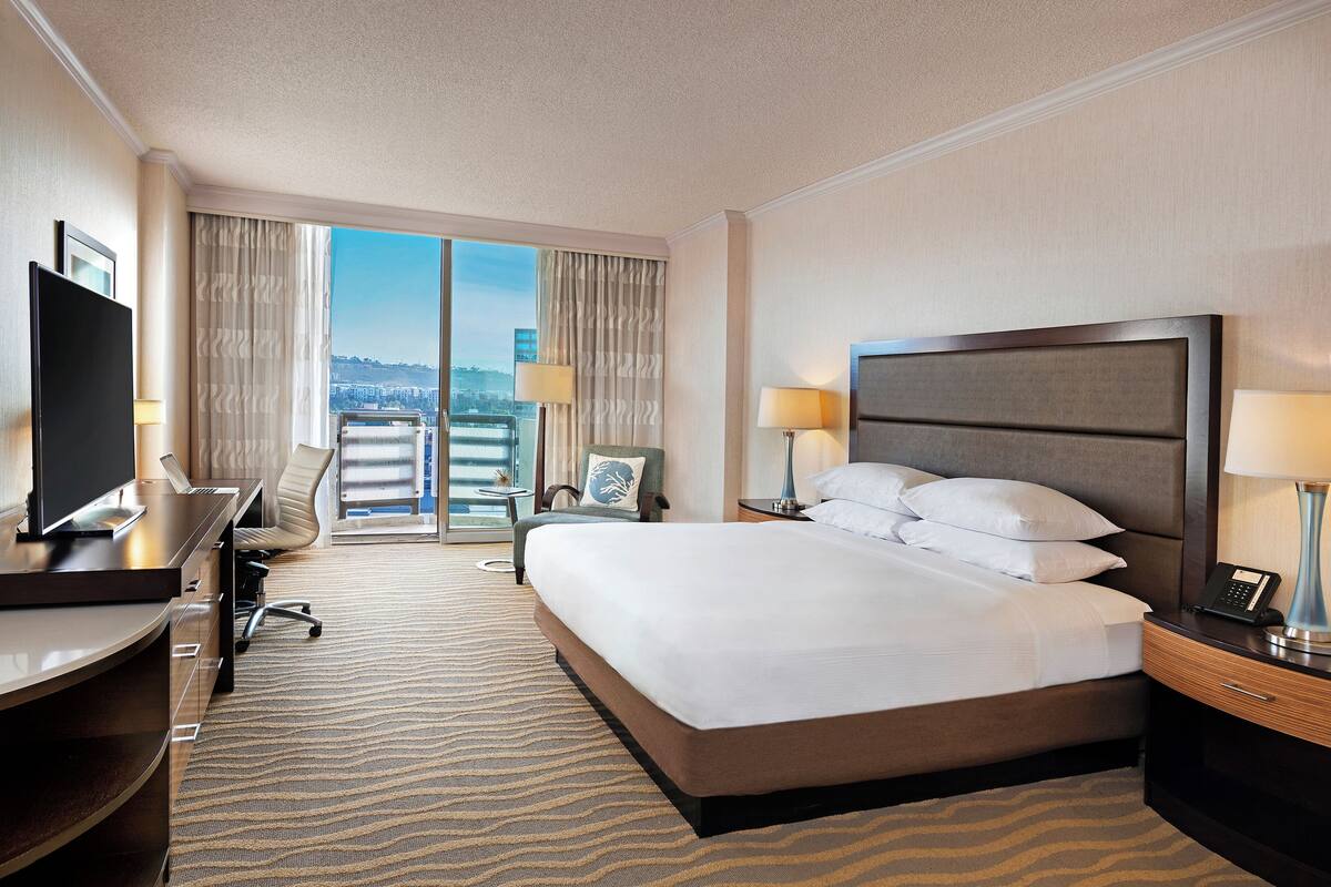 Habitación de hotel con cama, escritorio, televisor y vista a la ciudad.
