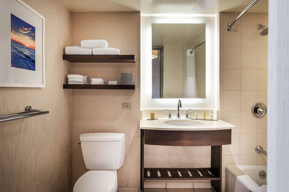 Un baño moderno con inodoro, lavabo con espejo, ducha y tozaleta con toallas.