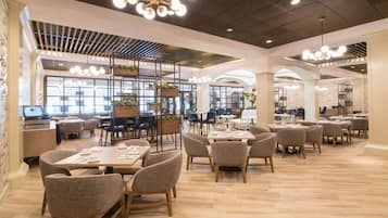 A spacious restaurant with high ceilings, modern chandeliers, and a mix of seating arrangements including tables and chairs.