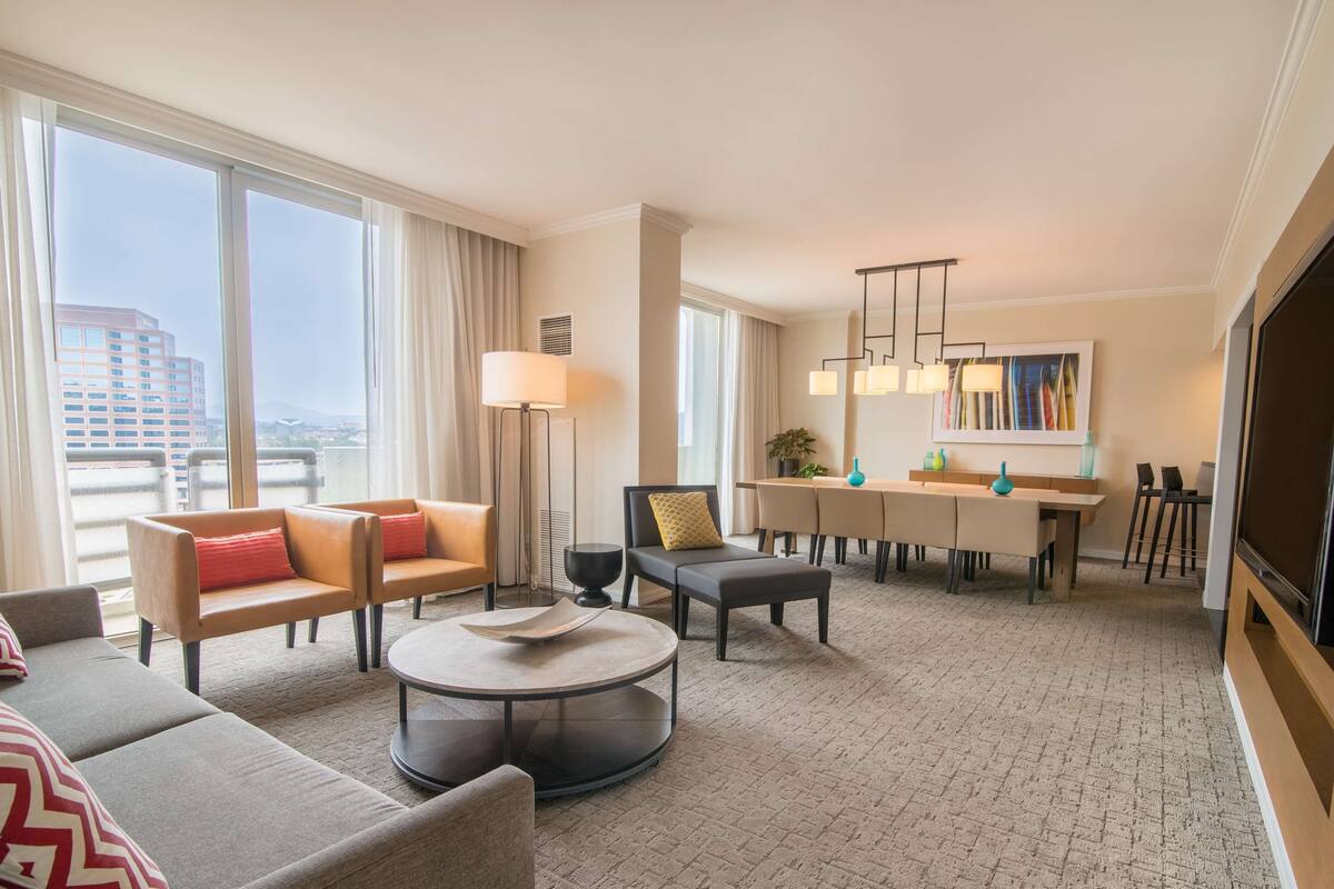 Una habitación de hotel moderna con zona de estar, comedor y un televisor grande.