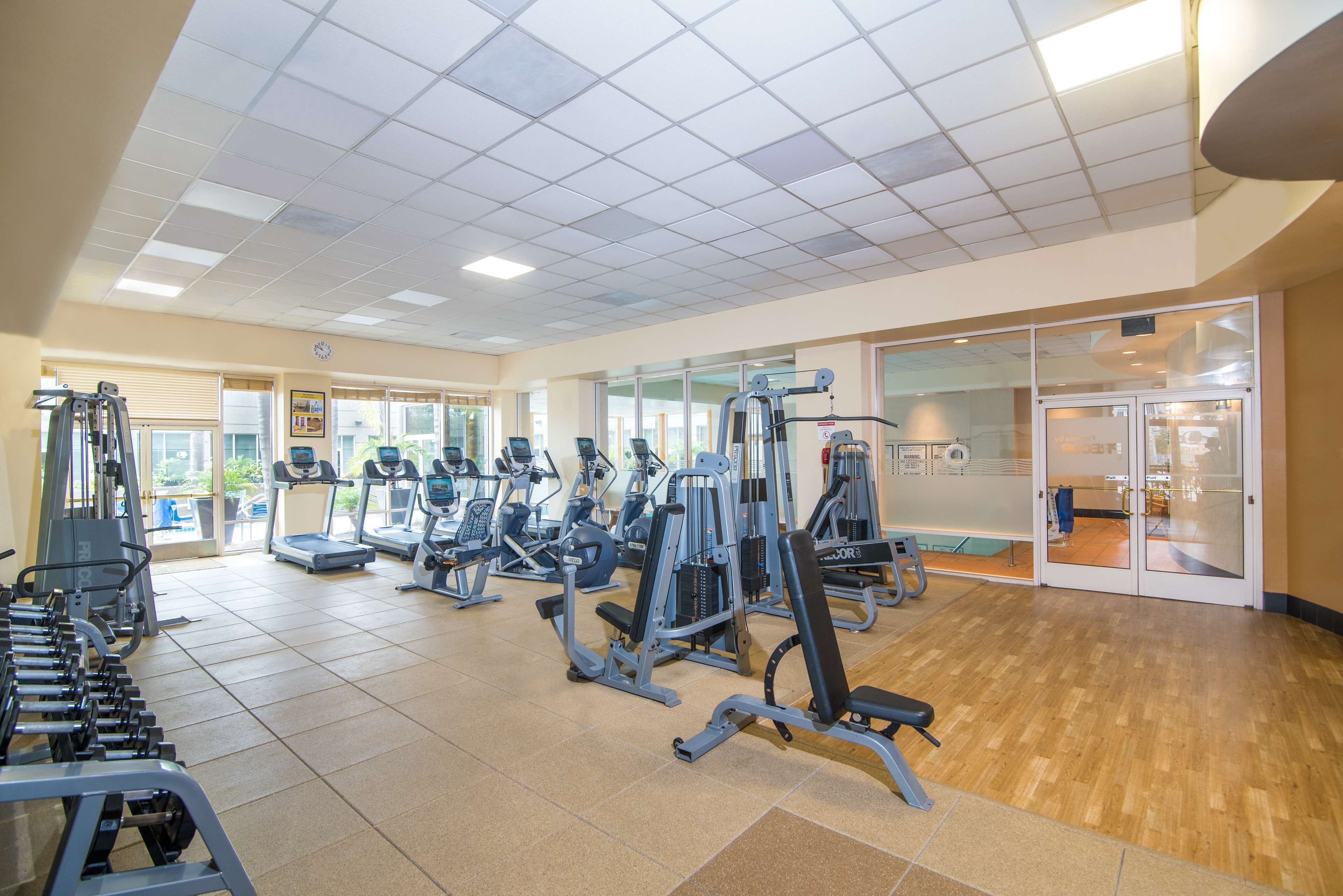 A gym with various exercise machines, a wooden floor, and a large window.