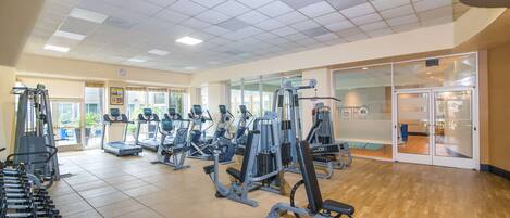 A gym with various exercise machines, a wooden floor, and a large window.