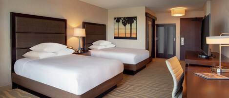 A hotel room with two beds, a desk, a chair, a lamp, and a painting on the wall.
