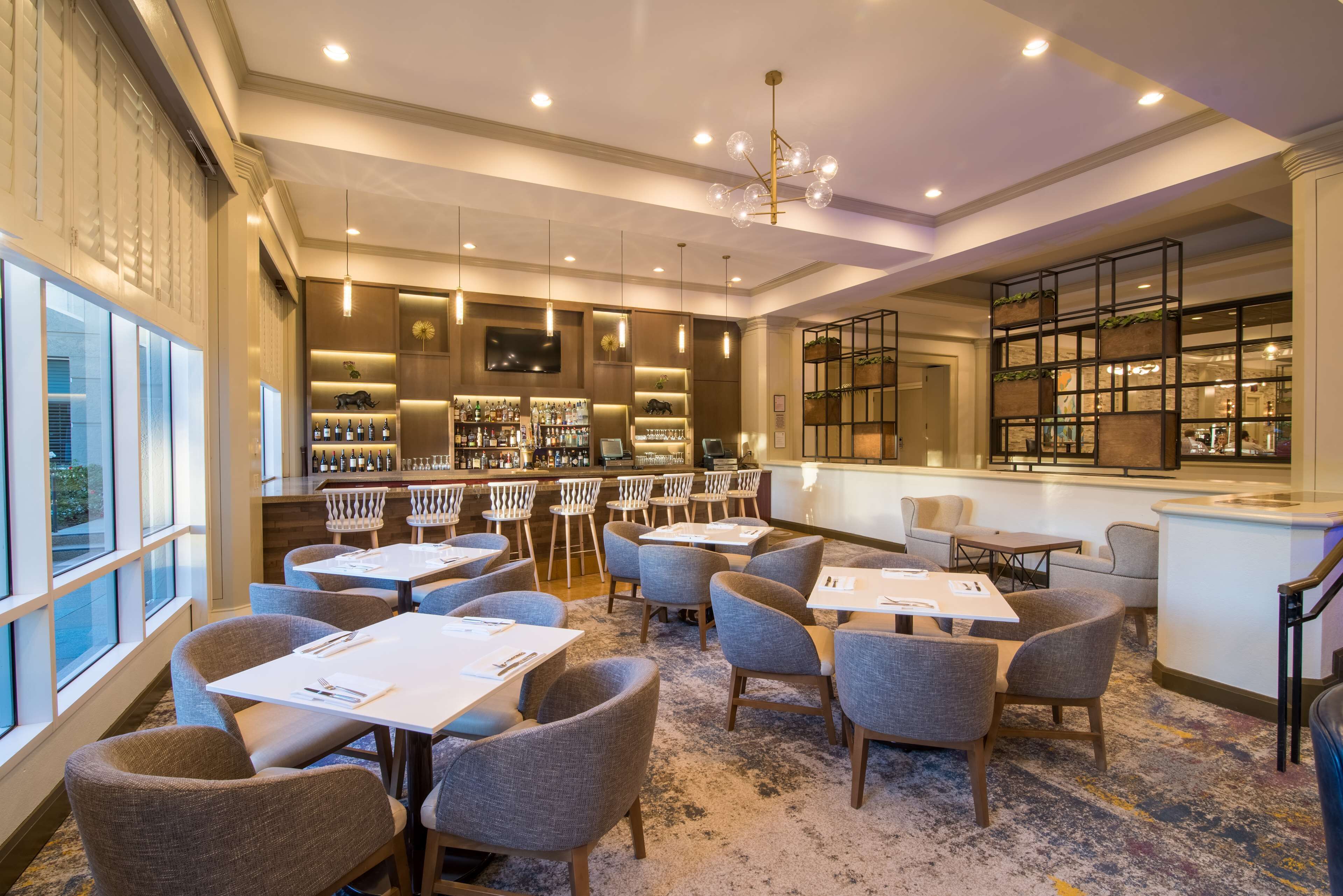 A modern hotel lobby with a bar area, seating arrangements, and a large window providing a view.