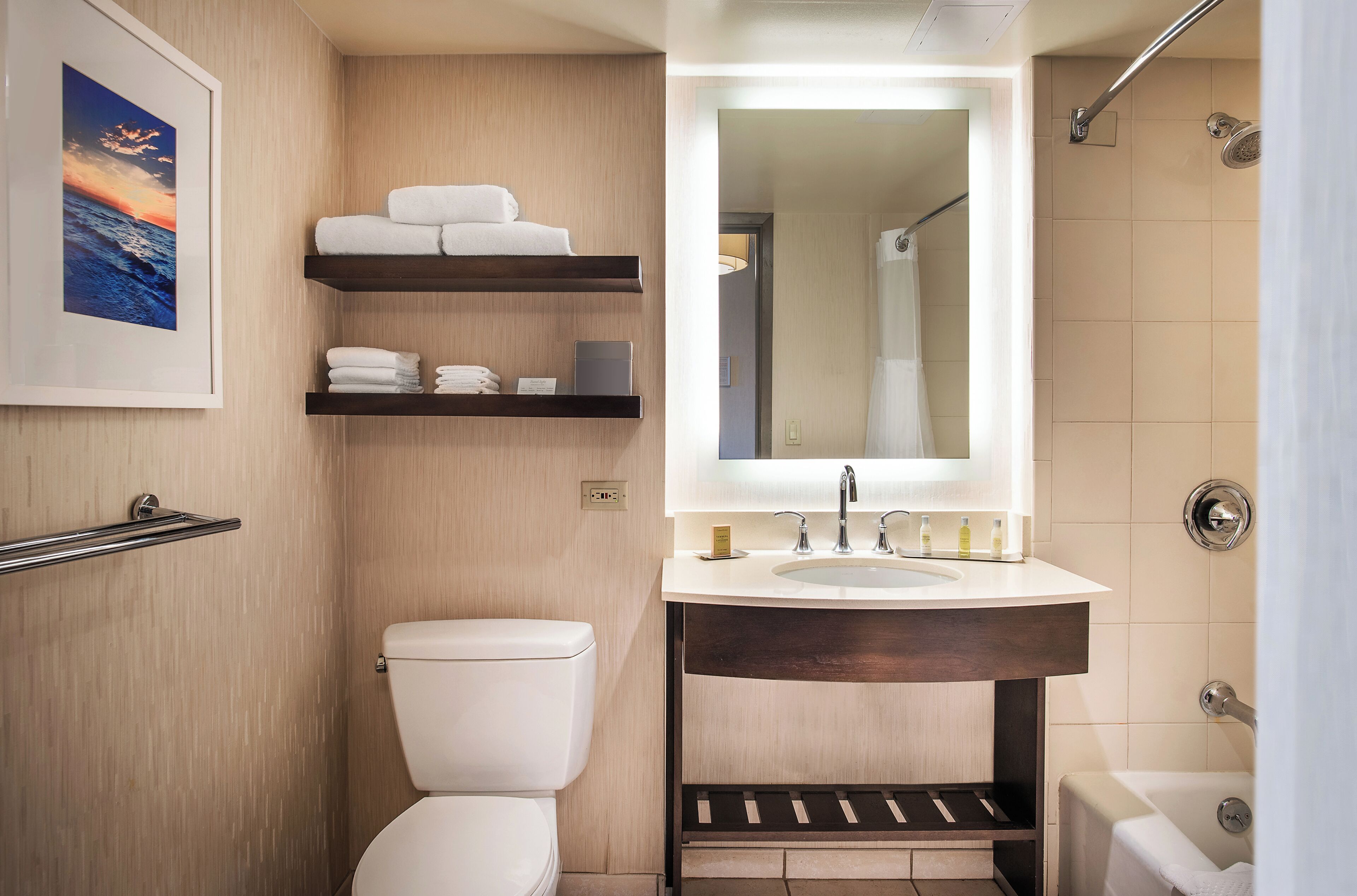 Een badkamer met toilet, wastafel met spiegel, douche en planken met handdoeken.