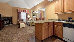 A compact kitchen with wooden cabinets, a built-in dishwasher, and a small island with a sink. - Homewood Suites by Hilton Syracuse/Liverpool (Liverpool)