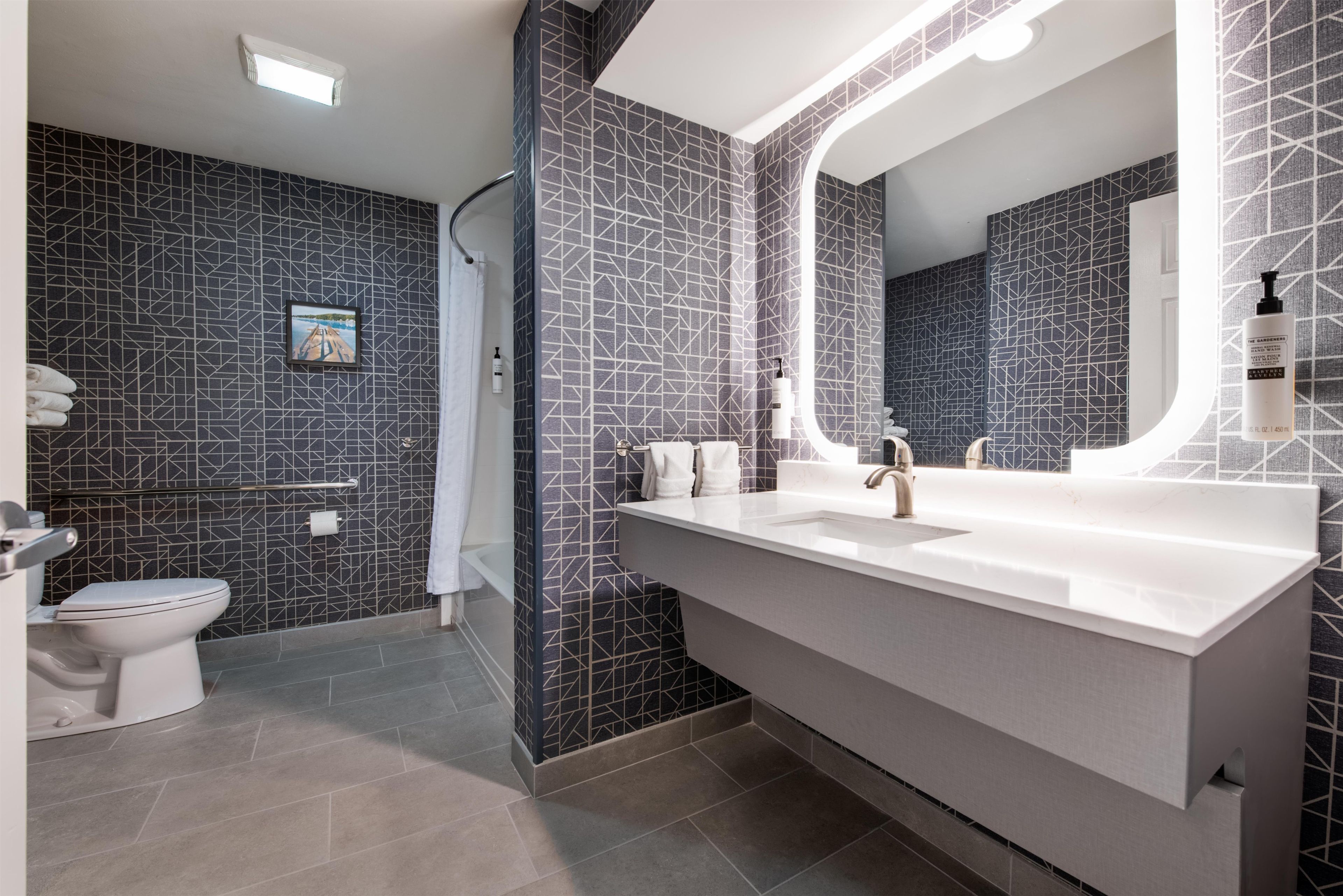 A modern bathroom with a large mirror, a white sink, and a shower area.
