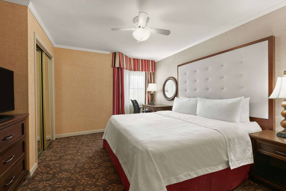 A hotel room with a bed, a television, a desk, and a ceiling fan.