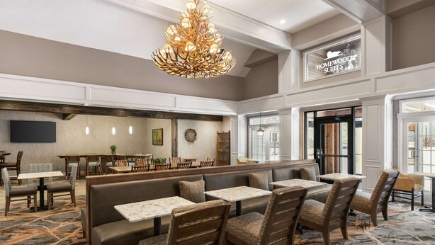 A hotel lobby with a seating area, a large chandelier, a clock, and a sign for Homewood Suites. - Homewood Suites by Hilton Syracuse/Liverpool (Liverpool)