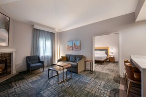 A hotel room with a sofa, armchair, small table, and a bed with a nightstand. - Homewood Suites by Hilton Syracuse/Liverpool (Liverpool)
