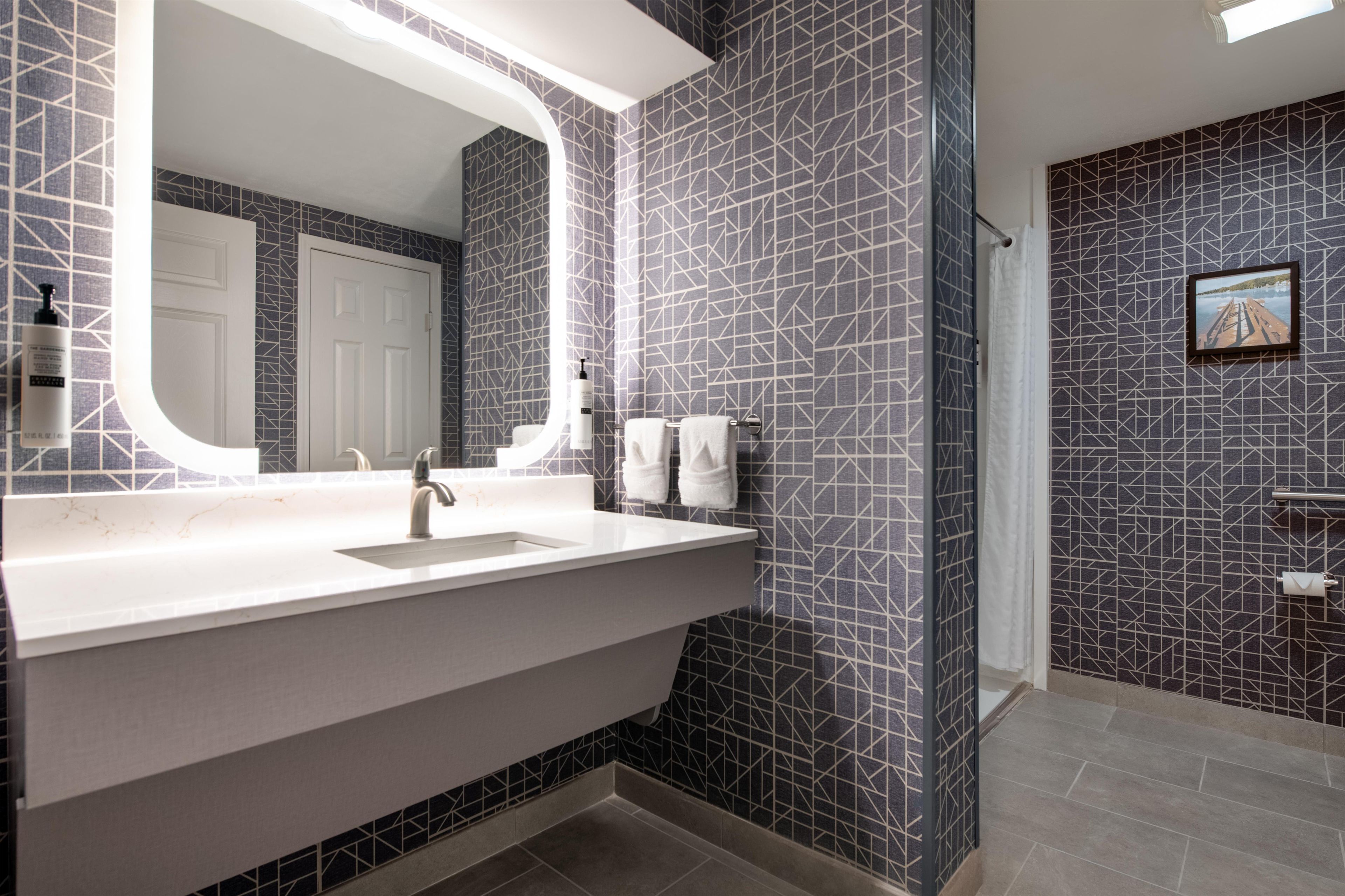 A bathroom with a large mirror, a sink, and a shower area.