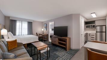 A hotel room with a bed, a desk, a television, a kitchenette, and a seating area.