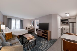 A hotel room with a bed, a desk, a television, a kitchenette, and a seating area.