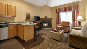 A compact living space with a kitchen, dining area, and seating area. It includes a fireplace, a television, and a lamp. - Homewood Suites by Hilton Syracuse/Liverpool (Liverpool)