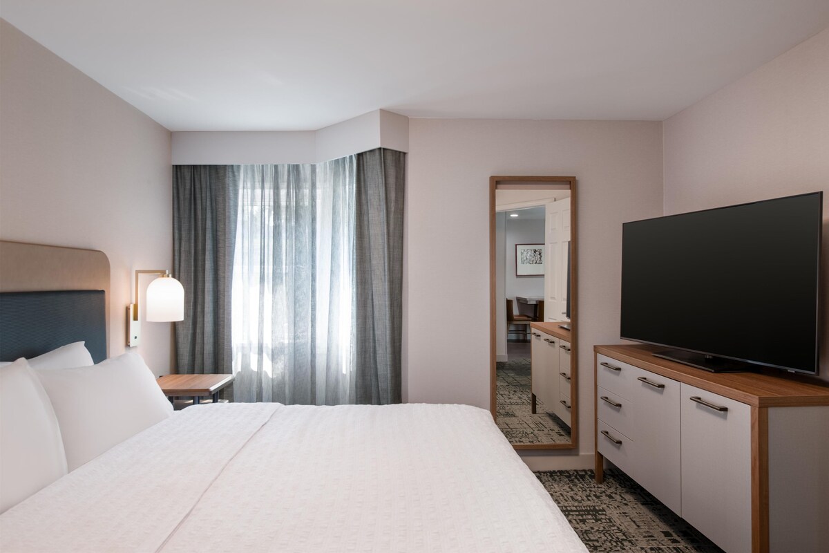 A hotel room with a bed, a television, a desk, and a mirror.