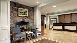 A lobby with a stone fireplace, seating area, and a reception desk. - Homewood Suites by Hilton Syracuse/Liverpool (Liverpool)