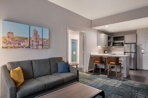 Una sala moderna con un sofá gris, una mesa de centro y una pintura de un paisaje urbano en la pared.