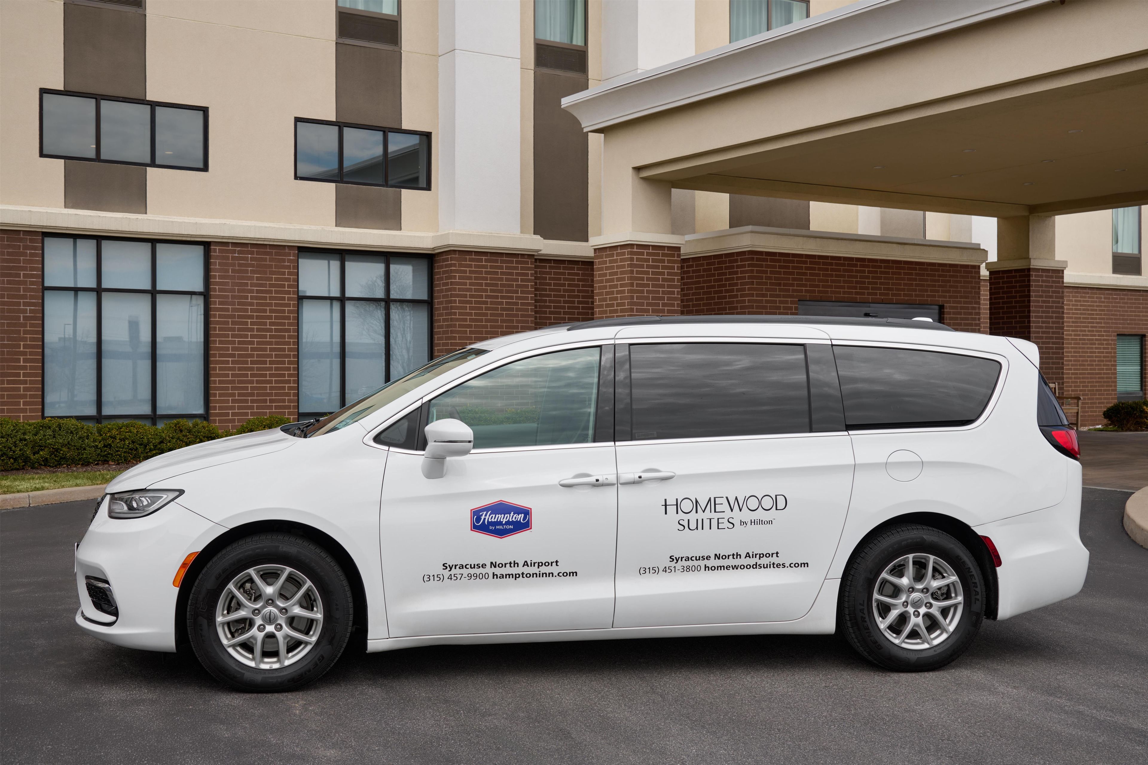 A white van parked in front of a building with a brick facade and large windows.