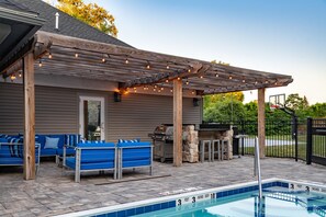 A poolside area with a covered seating area, a barbecue grill, and a stone wall. - Homewood Suites by Hilton Syracuse/Liverpool (Liverpool)