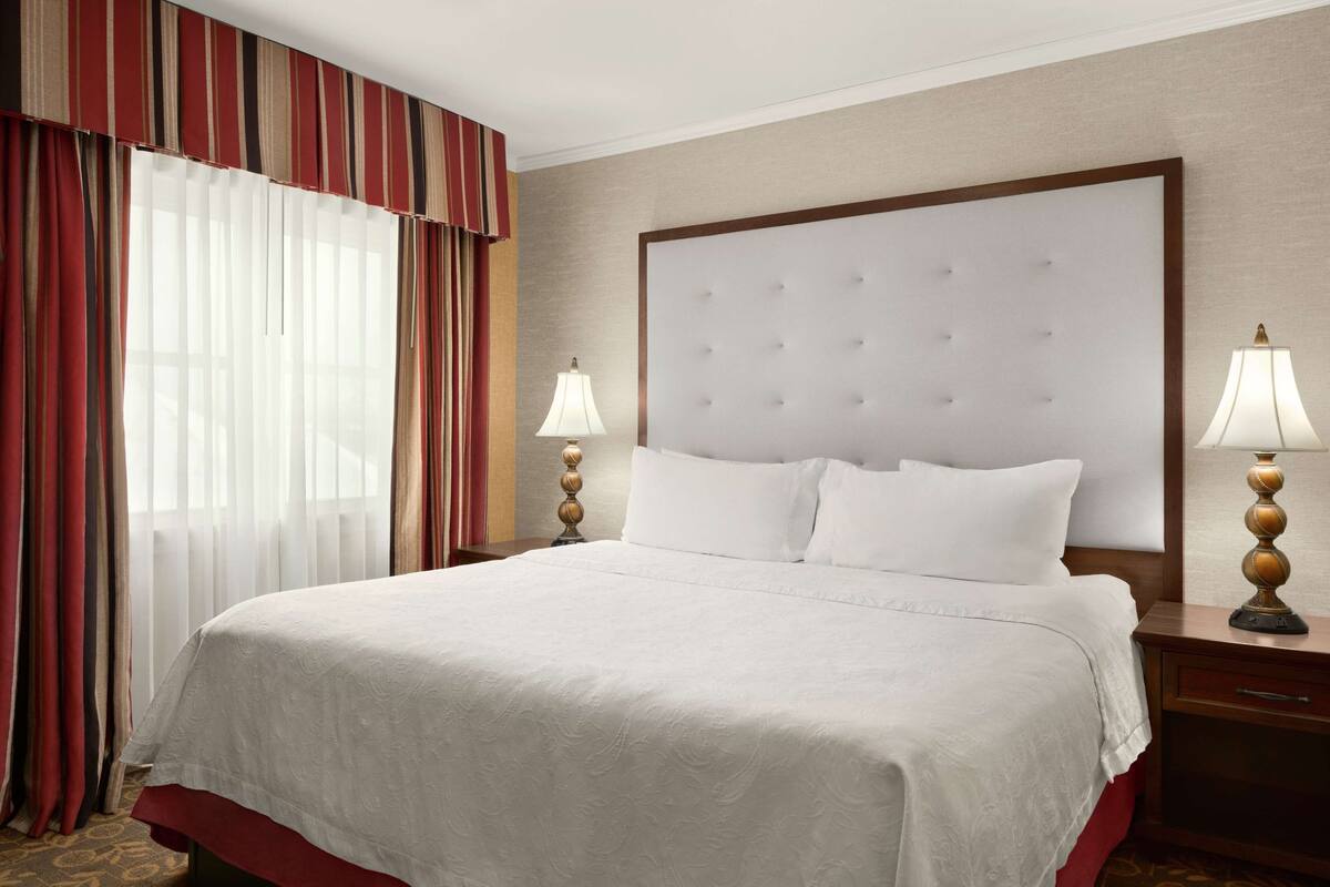 A hotel room with a large bed, two bedside lamps, and a window with curtains.